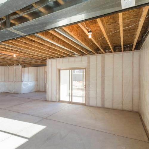 A basement mid-project: framing and insulation exposed, floor protection down