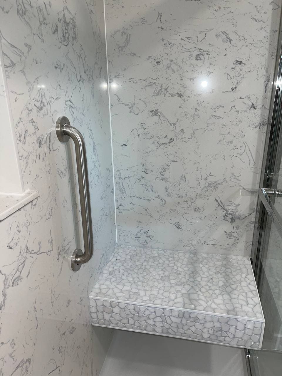 Marble-look shower with a tiled bench seat and grab bar