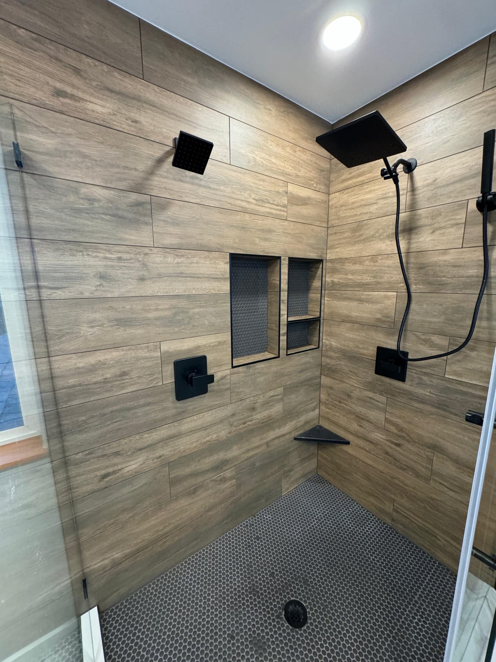 Finished walk-in shower: wood-look large-format tile floor to ceiling, rain head and handheld in matte black, tiled niches