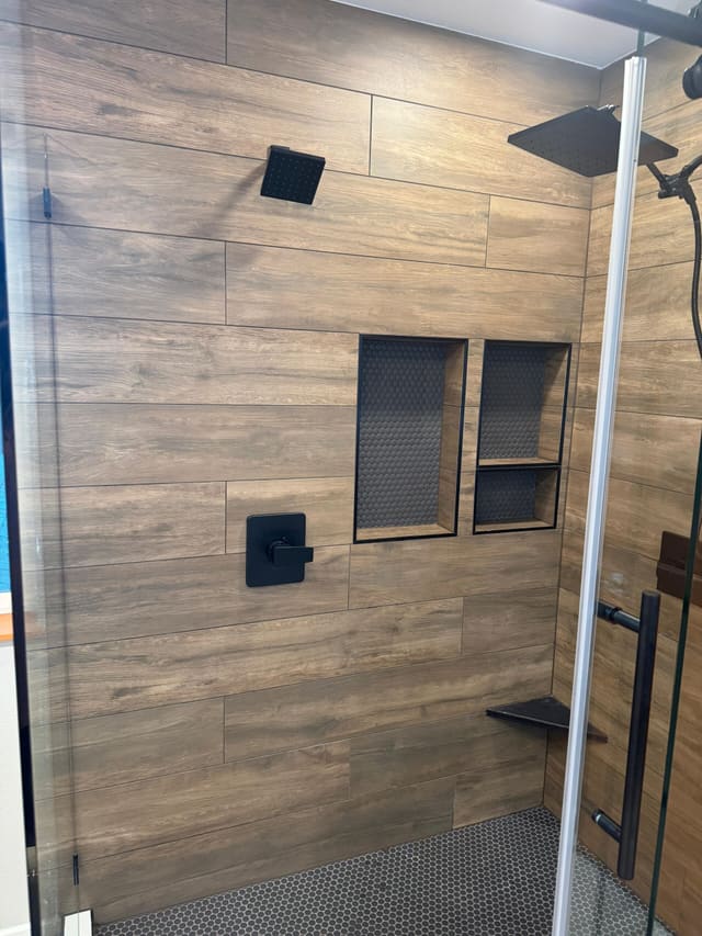 Side view of the tiled shower wall: wood-look plank tile, matte-black valve, two recessed niches