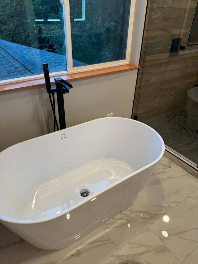 Freestanding white tub with a floor-mounted matte-black filler, glass shower enclosure behind